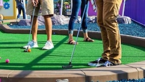 Un camp de mini golf amb superfície de joc verda, tanca morada i un element decoratiu blau al primer pla.