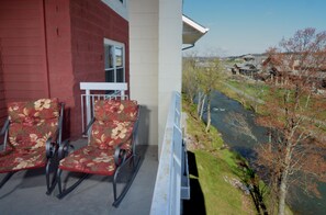 Een balkon met twee schommelstoelen, een rode bakstenen muur en een uitzicht op een rivier en huizen in de verte.