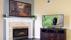 A living room with a fireplace, a mounted painting, a television, and a dark wooden entertainment center. - Bear Crossing 402 (Pigeon Forge)