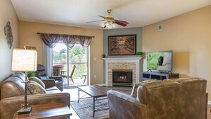 A living room with a fireplace, leather sofas, a coffee table, a TV, and a balcony with curtains. - Bear Crossing 402 (Pigeon Forge)