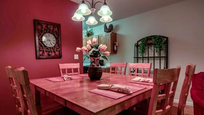 Une salle à manger avec une table en bois dressée pour quatre personnes, des sets de table roses et un vase rempli de fleurs roses.