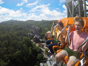 A roller coaster with passengers seated in orange chairs, surrounded by lush greenery and a clear sky. - Bear Crossing 502 (Pigeon Forge)