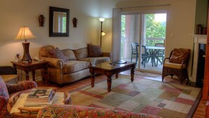 A cozy living room with a sofa, a coffee table, and a patterned rug. There is a dining area with chairs and a table visible through a glass door. - Bear Crossing 401 (Pigeon Forge)