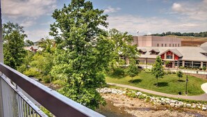 Uitzicht vanaf een balkon over een rivier, een gebouw met een rode gevel en een grote boom op de voorgrond.