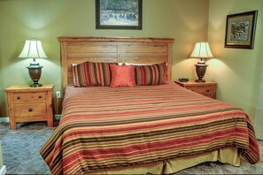 Une chambre à coucher avec une tête de lit en bois, une couvre-lit à rayures, deux tables de chevet avec des lampes et un tableau encadré au mur.
