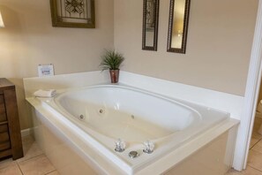 A large, white bathtub with two faucets and a small potted plant beside it.