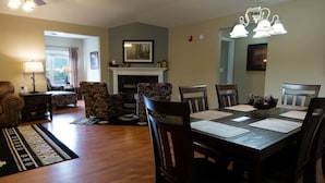 A dining area with a wooden table, chairs, and a chandelier. There is a fireplace with a mantel and framed pictures above it. - Bear Crossing 501 (Pigeon Forge)