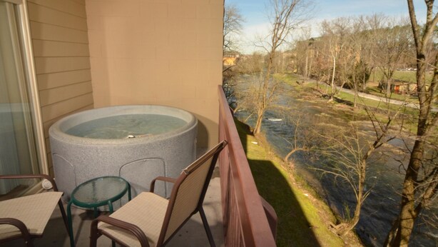 A balcony with a hot tub, chairs, and a view of a river and trees.
