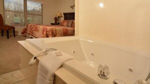 A bathroom with a large bathtub, a chair, and a bed with a floral bedspread.