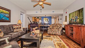 A spacious living room with a ceiling fan, a large TV, and a dining area in the background. - Cedar Lodge 105 (Pigeon Forge)