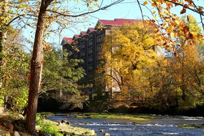 A river flowing through a wooded area with autumn foliage and a building with a red roof in the background. - Cedar Lodge 105 (Pigeon Forge)