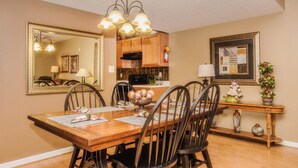 A dining area with a wooden table, chairs, a chandelier, and kitchen cabinets in the background.