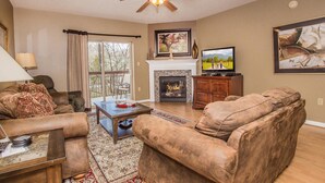 A living room with a fireplace, a ceiling fan, and a television.