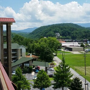 A view of a parking lot with several cars, a building with a green roof, and a mountainous landscape in the background.