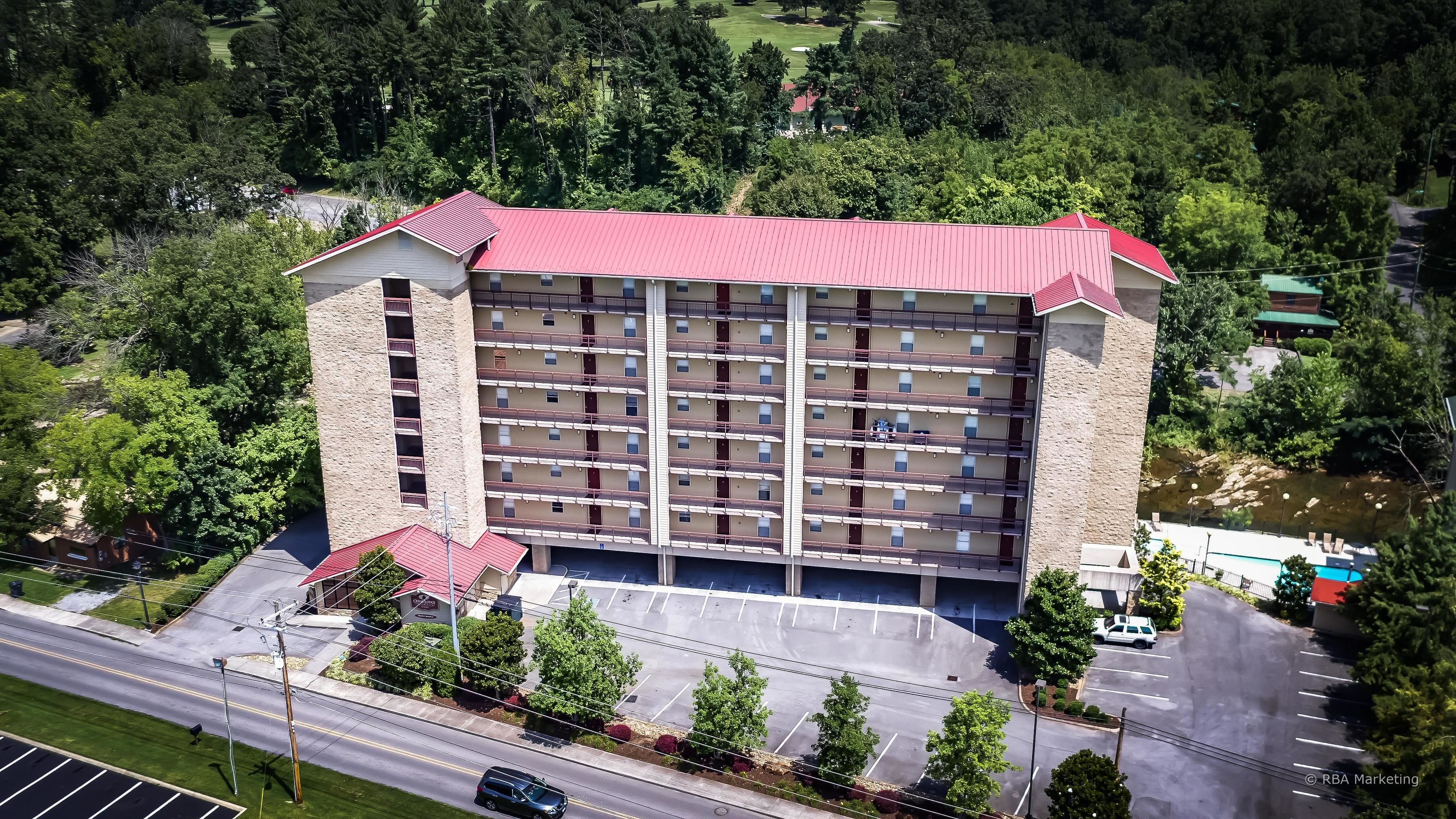 Ein mehrstöckiges Hotel mit rotem Dach, umgeben von Grünflächen und einem Parkplatz.