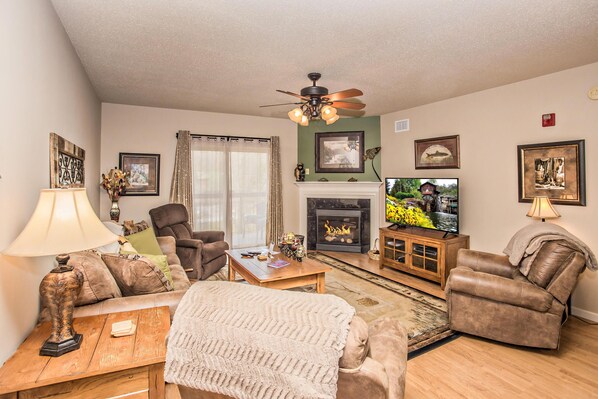 A living room with a fireplace, a television, and a ceiling fan.