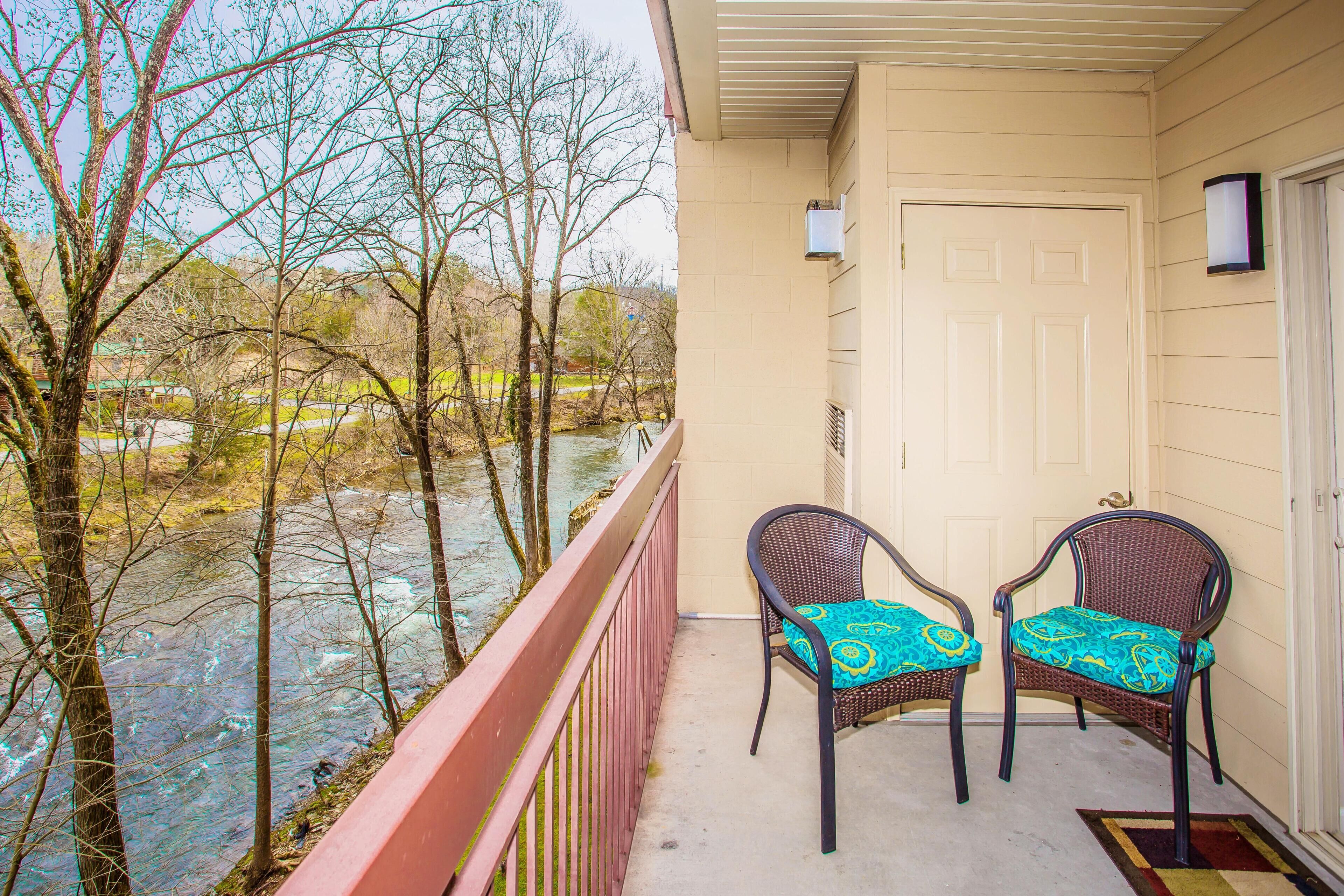 A balcony with two wicker chairs, a view of a river, and a door with a light fixture.