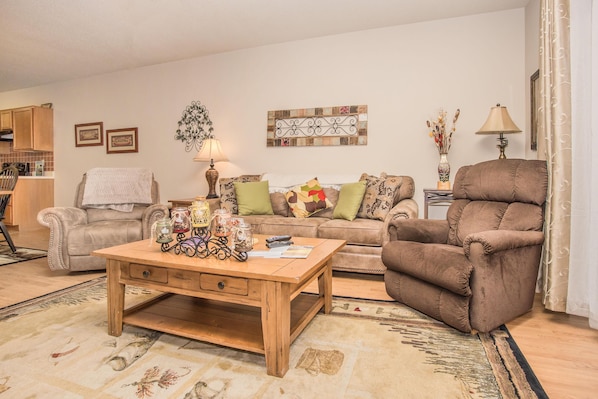 A living room with a beige sofa, a brown recliner, a wooden coffee table, and a patterned rug.