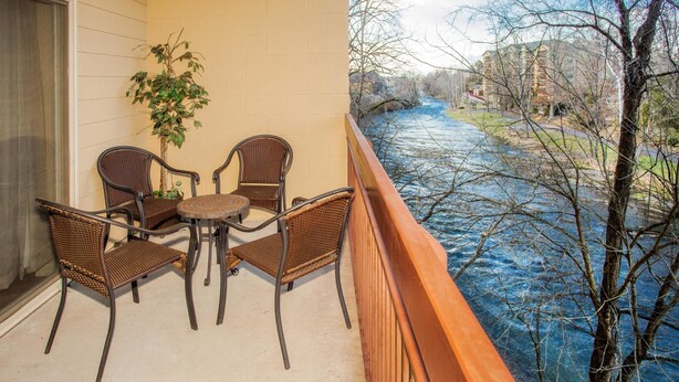 Een balkon met rieten stoelen en een tafeltje, met uitzicht op een rivier en gebouwen op de achtergrond.