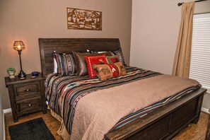 A bedroom with a wooden bed, patterned bedding, a nightstand with a lamp, and a wall-mounted artwork. - Cedar Lodge 402 (Pigeon Forge)