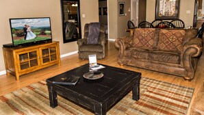 A living room with a television, a wooden cabinet, a black coffee table, a patterned sofa, and a dining area in the background. - Cedar Lodge 302 (Pigeon Forge)