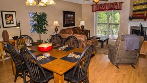 A dining area with a wooden table, black chairs, and a red bowl. There is a sofa with a patterned throw, a lamp, and a plant. - Cedar Lodge 302 (Pigeon Forge)