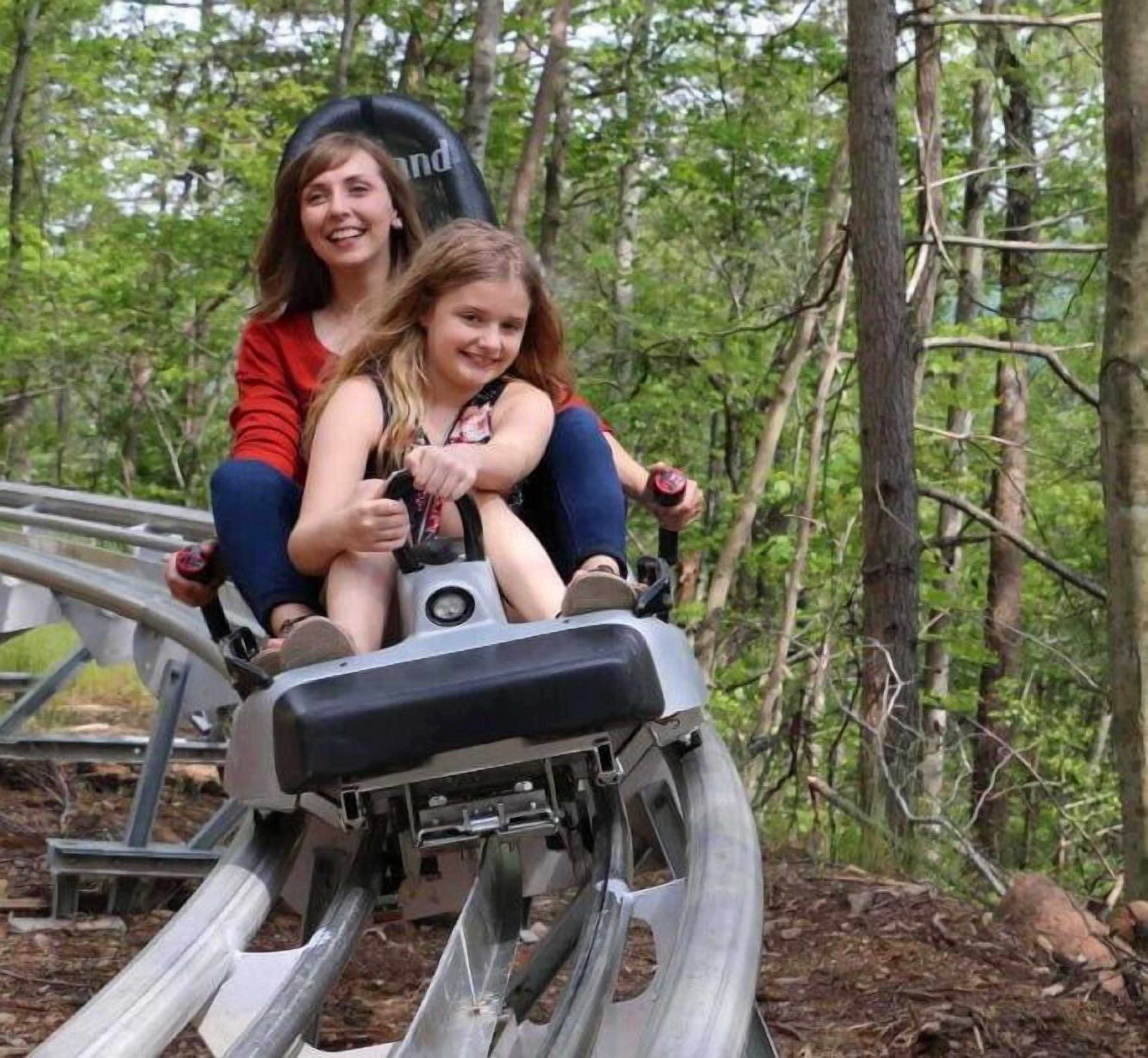 Two people on a wooden roller coaster in a forested area.
