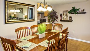 A dining area with a wooden table and chairs, a mirror, and a kitchen in the background. - Cedar Lodge 301 (Pigeon Forge)