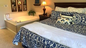 A bedroom with a large bed, a bedside table with a lamp, a decorative mirror, and a bathtub. - Cedar Lodge 301 (Pigeon Forge)