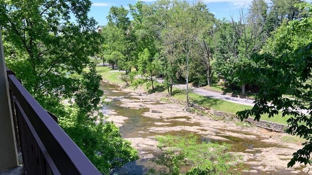 A river with a rocky bed, surrounded by trees and a building in the background. - Cedar Lodge 301 (Pigeon Forge)