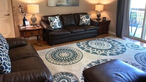 A living room with a leather sofa, patterned throw pillows, and a large decorative rug. There are two lamps on side tables, and a painting hangs on the wall. - Cedar Lodge 301 (Pigeon Forge)