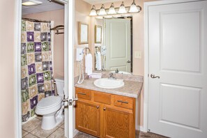 A bathroom with a toilet, sink, vanity, and a shower curtain.