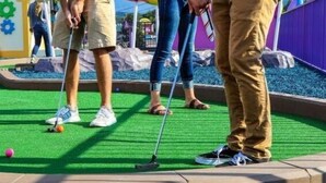 Ein Minigolfplatz mit grüner Spielbahn, einem Putting-Loch und einem lila Zaun im Hintergrund.