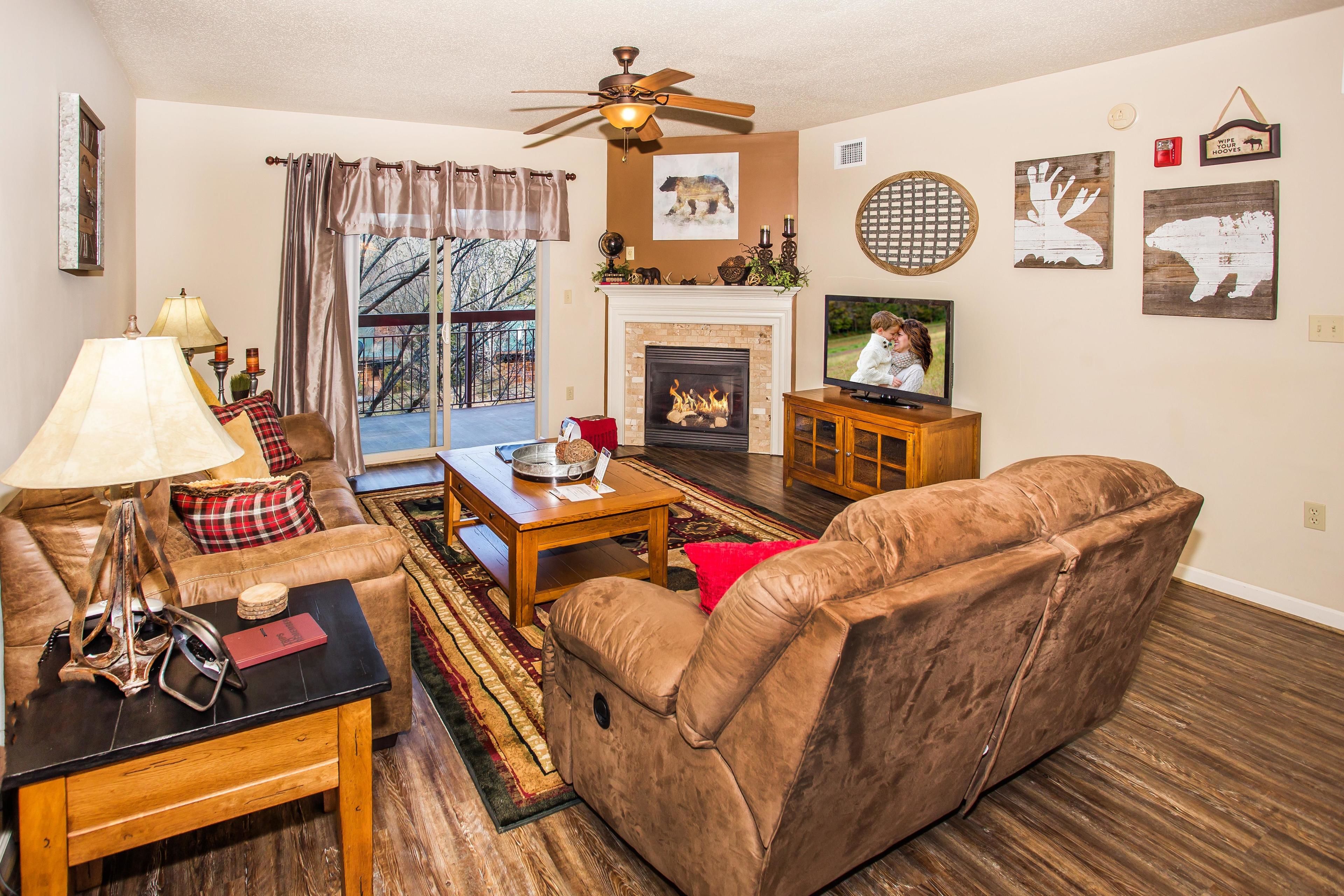 A living room with a sofa, coffee table, and fireplace. There is a television on a stand and a ceiling fan.