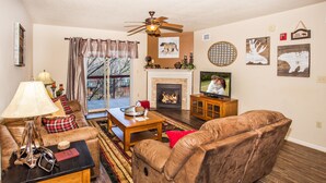 Ein Wohnzimmer mit Sofa, Couchtisch und Kamin. Ein Fernseher steht auf einem Lowboard und ein Deckenventilator ist angebracht.