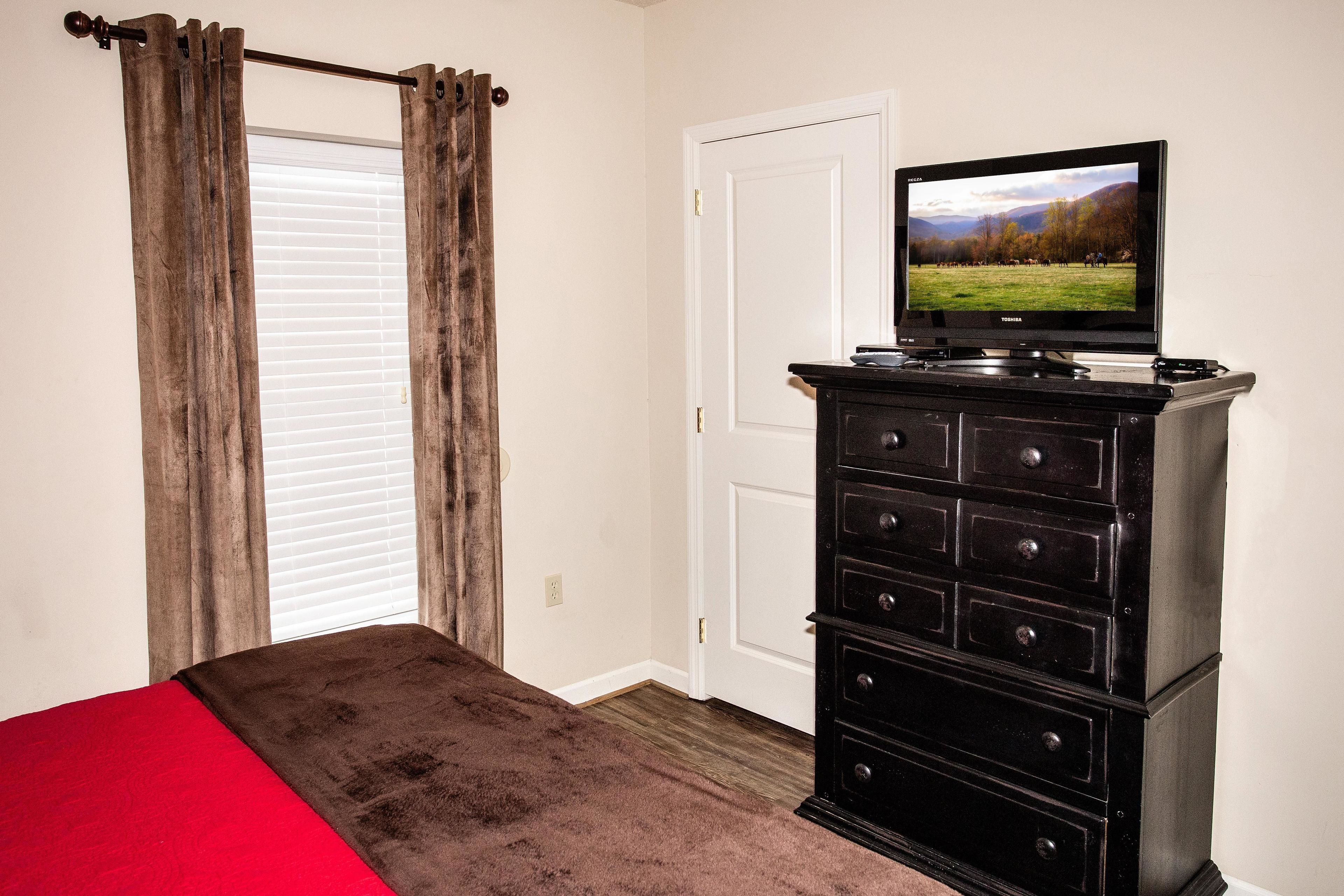 A bedroom with a bed, a dresser, and a television on a dresser.