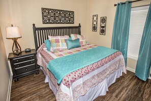Un dormitorio con cama, mesita de noche, lámpara, cómoda y ventana con cortinas.