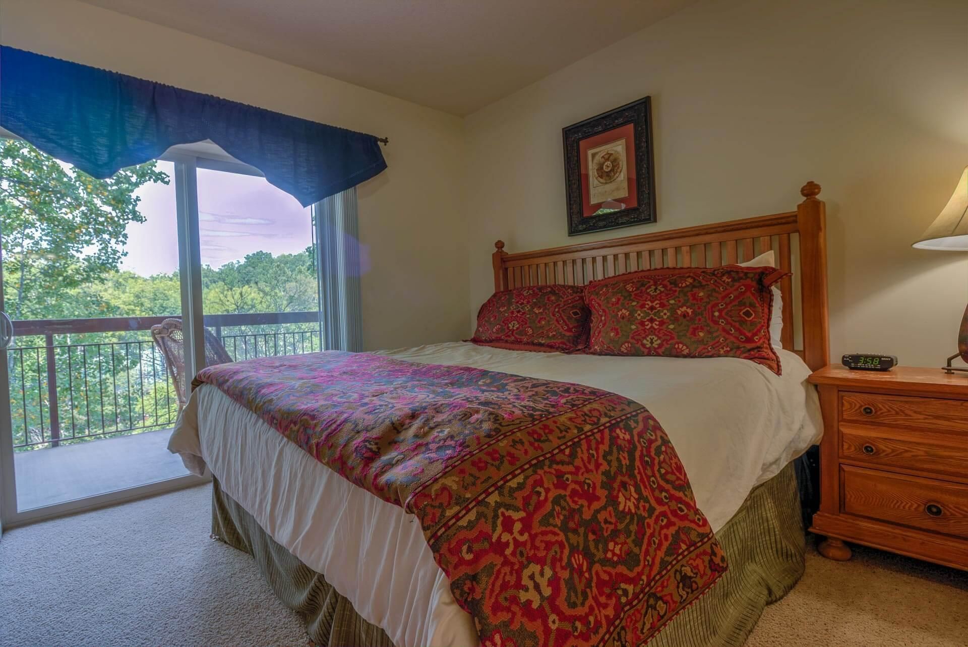 A bedroom with a bed, a nightstand, a dresser, a window with a view, and a framed picture on the wall.