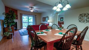 A dining area with a wooden table and chairs, a ceiling fan, and a large window with curtains. - Cedar Lodge 405 (Pigeon Forge)