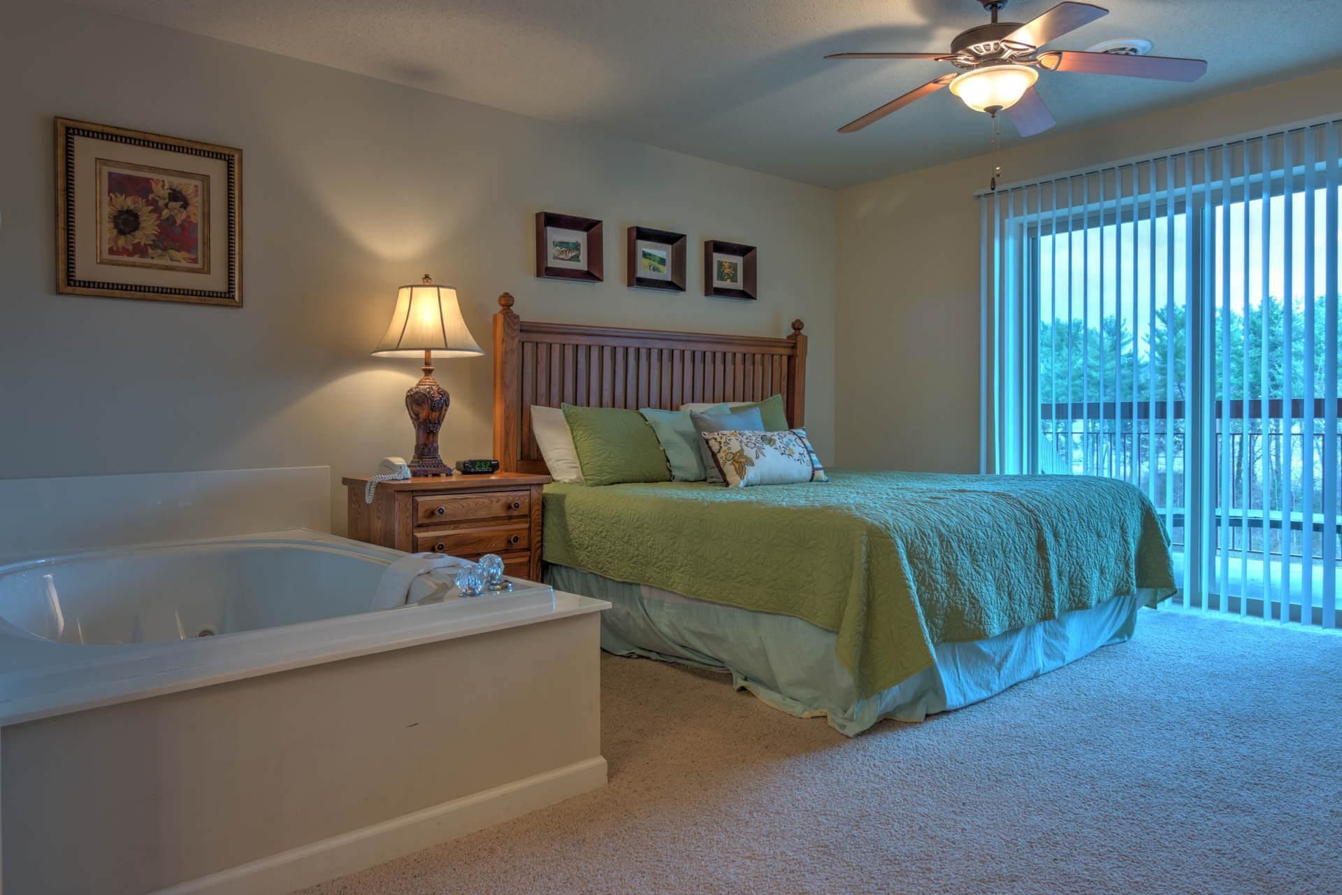 A bedroom with a large bed, a nightstand with a lamp, a wooden headboard, and a ceiling fan.