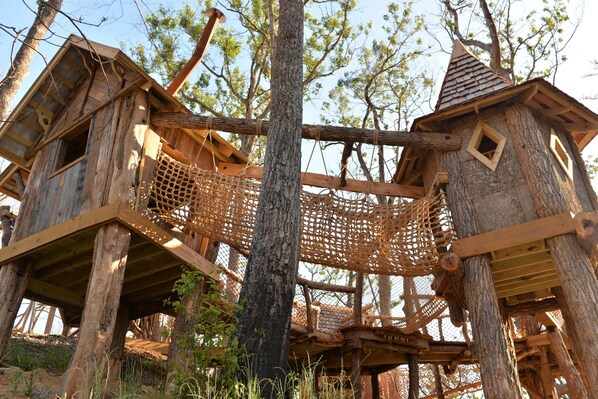 A wooden treehouse structure with a rope bridge, surrounded by trees.
