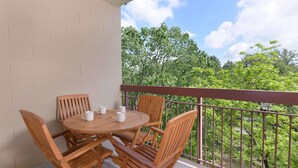 A wooden table and chairs on a balcony with a view of trees and a clear sky.