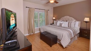 A bedroom with a bed, a TV, a ceiling fan, and a window with curtains.