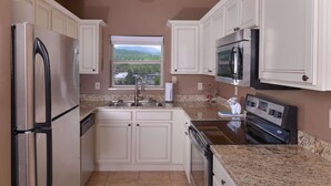 A kitchen with white cabinets, stainless steel appliances, a granite countertop, and a window with a view of mountains.