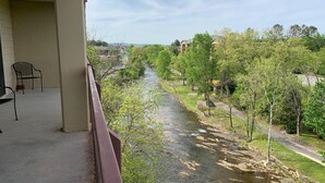 A balcony with a view of a river, trees, and buildings in the background.