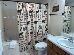 Ein Badezimmer mit Duschvorhang, der einen Elch und Blättermuster zeigt, einer Toilette, einem Waschbecken und einem Holzschrank.
