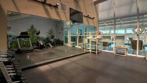A gym with exercise equipment, a large mirror, and a view of a pool through large windows. - Whispering Pines 111 (Pigeon Forge)