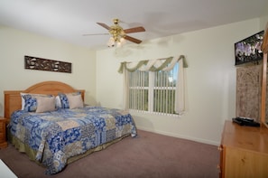 A bedroom with a bed, a ceiling fan, a window with curtains, and a wooden dresser.