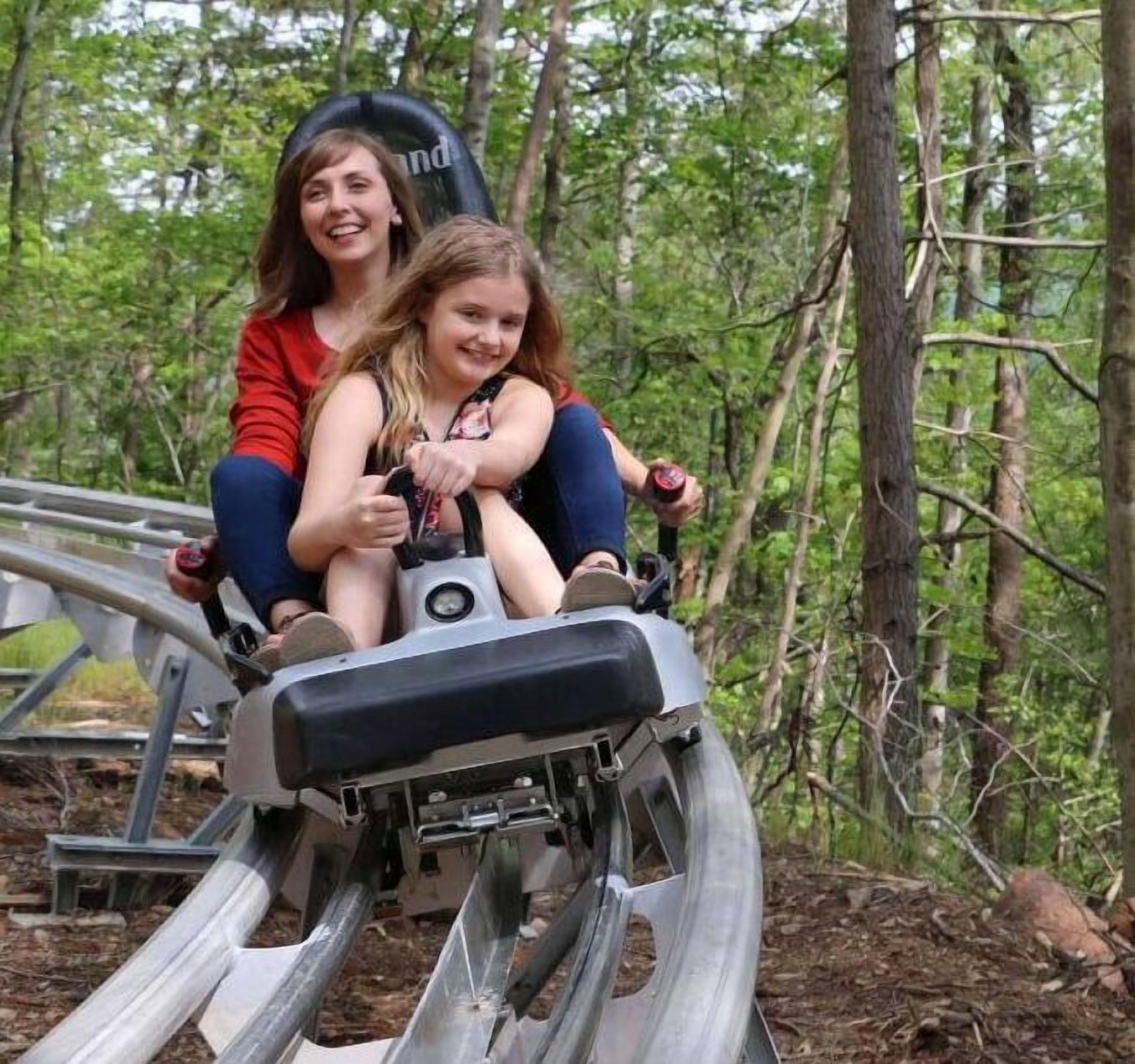Two people on a wooden roller coaster track in a wooded area.