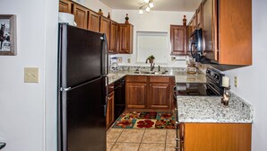 A kitchen with wooden cabinets, a black refrigerator, a granite countertop, and a floral-patterned rug. - Cedar Lodge 603 (Pigeon Forge)